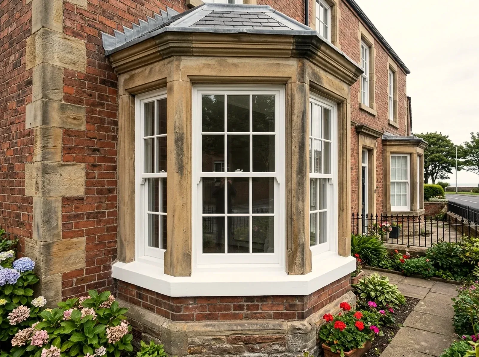 Victorian red-brick house with a carved sandstone bay of restored white box-sash windows above a front garden of hydrangeas