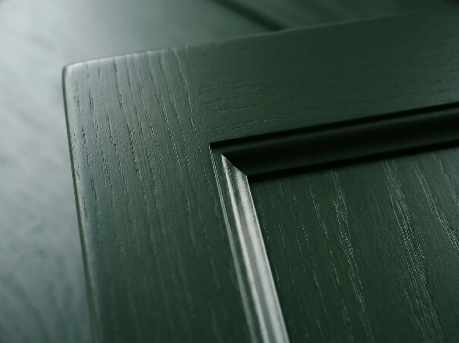 Close-up of a grain-filled oak Shaker door corner sprayed in deep green satin 2K polyurethane